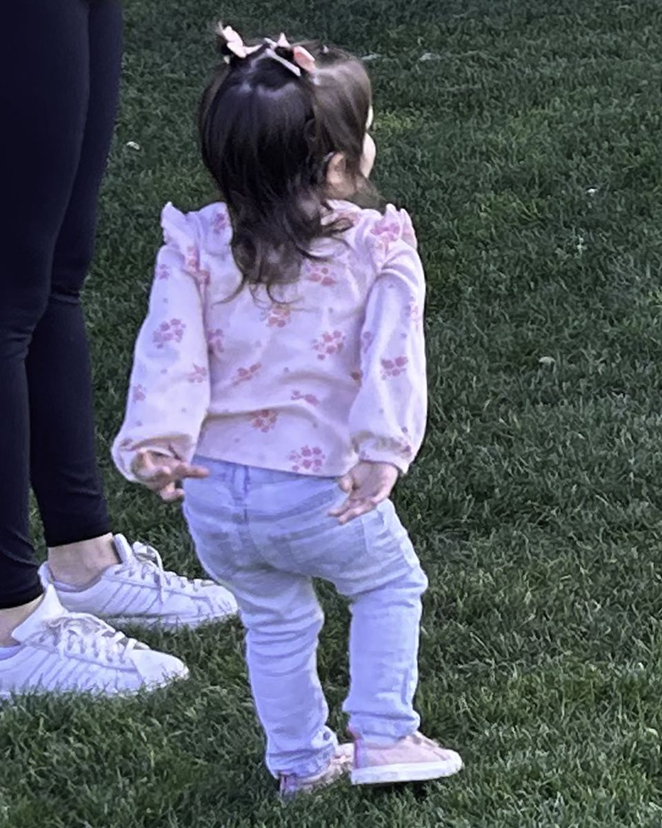 A toddler standing on the grass outdoors, listening at a distance.